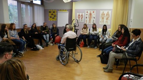 Ein Gruppe von Jugendlichen hören einem Mann im Rollstuhl zu