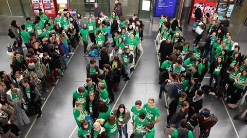 Verschiedene Personen mit grünen T-Shirts stehen auf einem Bahnhofsplatz