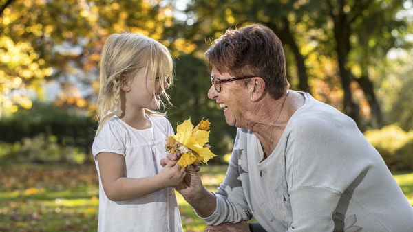 Lächelndes Mädchen mit Oma beim Blättersammeln im Herbst