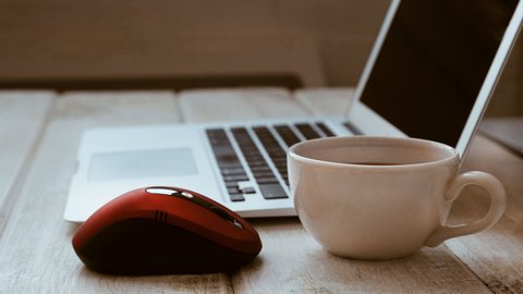 Kaffeetasse, rote Maus und Laptop auf einem Tisch