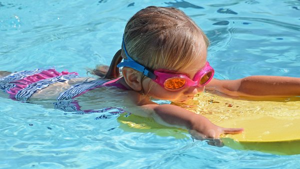 Ein kleines Kind mit Schwimmbrille im Pool beim Schwimmen