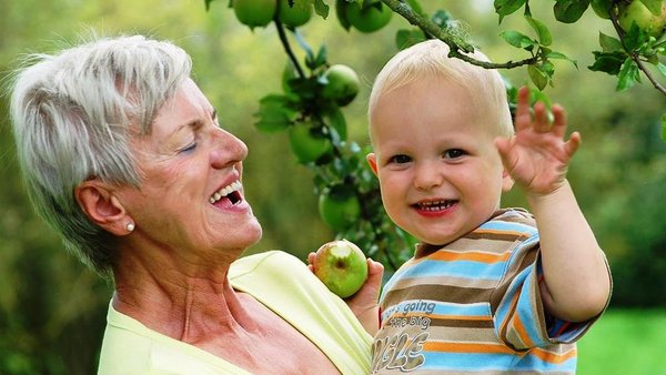 Oma mit Enkel, der einen angebissenen Apfel hält, im Obstgarten