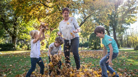 Drei Kinder spielen mit einer Oma mit Blättern im Herbst