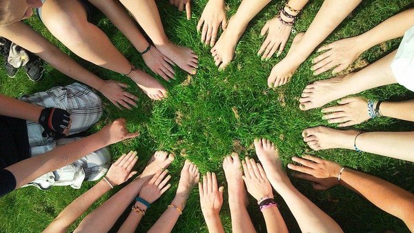 Viele Hände und Füße berühren einander im Kreis auf einem grünen Rasen