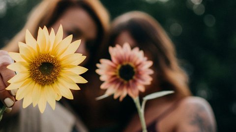 Foto mit zwei Frauen mit zwei Blumen, das Bild ist unscharf, man kann die Frauen nicht erkennen, die Blumen sind im Vordergrund