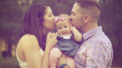 Zwei Eltern küssen ihr Baby am Kopf