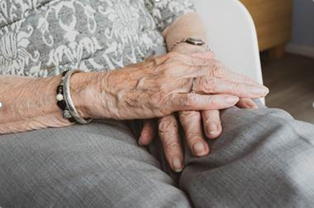 Seniorin faltet sitzend die Hände auf ihrem Schoß zusammen 
