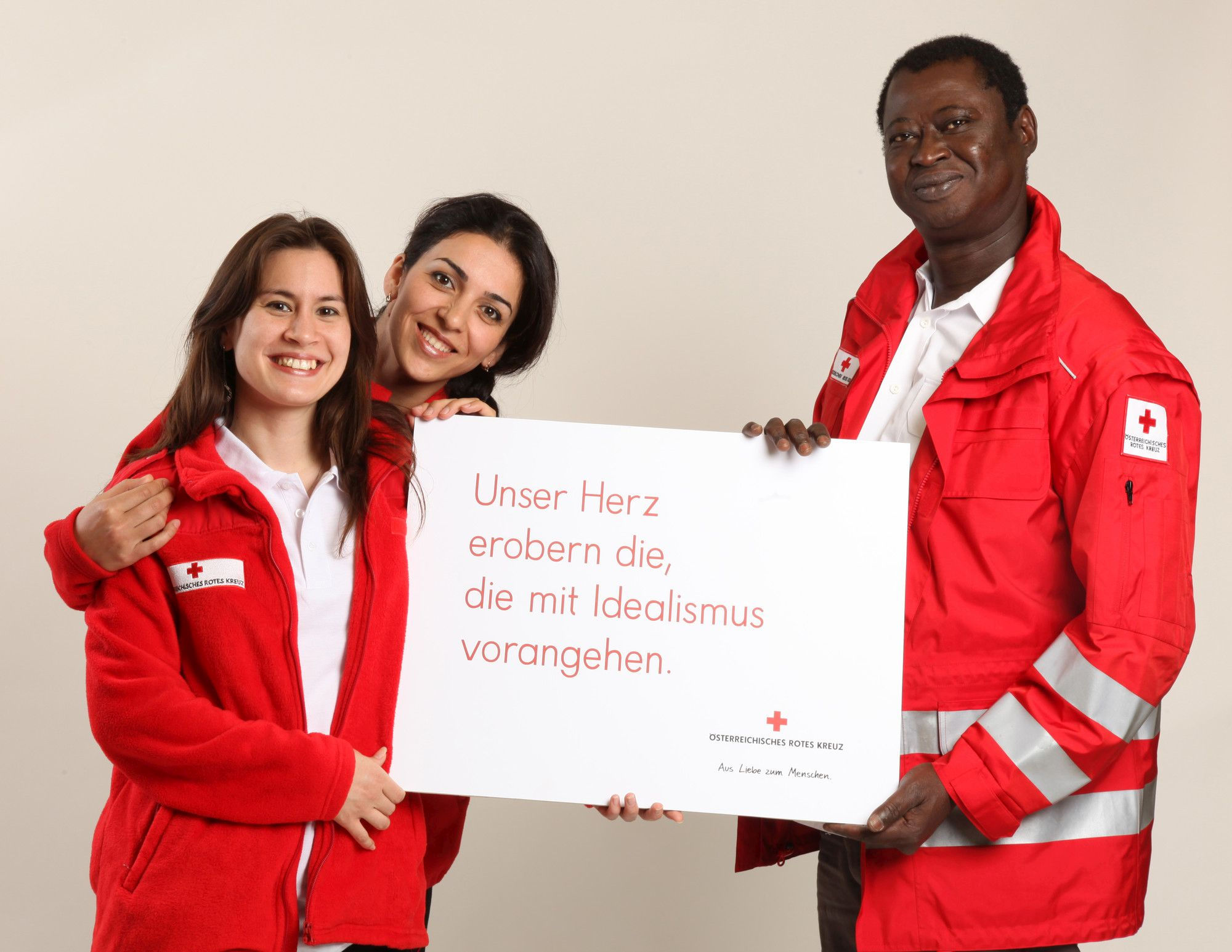 Drei Mitarbeiter vom Österreichischen Roten Kreuz halten Schild mit der Aufschrift "Unser Herz erobern die, die mit Idealismus vorangehen" in der Hand