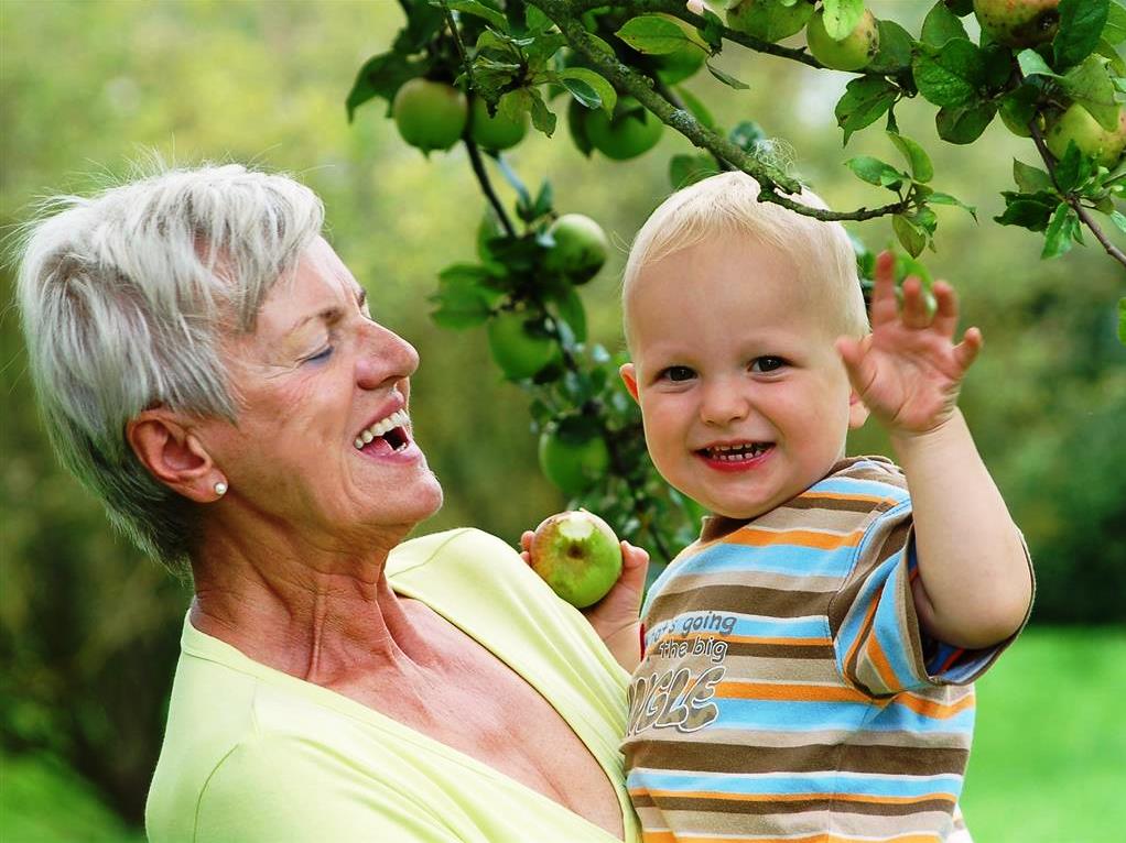 Oma mit Enkel, der einen angebissenen Apfel hält, im Obstgarten